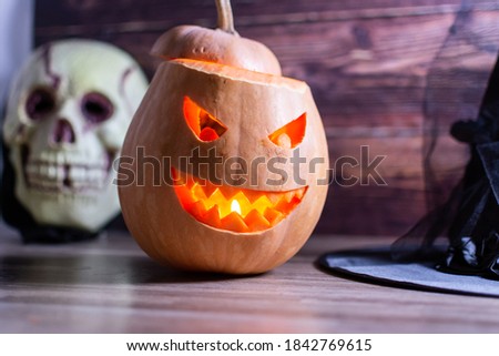 Halloween pumpkin lantern with skull and a witch's hat with wooden background. Halloween holiday concept with jack o lantern glitter pumpkin decor on wooden table.