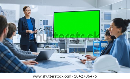Modern Industrial Factory Meeting: Confident Female Engineer Uses Interactive Green Mock-up Screen Whiteboard, Makes Report to a Group of Engineers, Managers