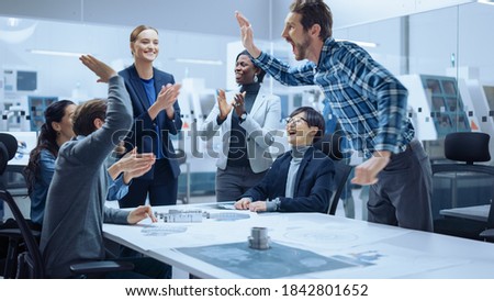Multi Ethnic Team of Industrial Engineers Standing at the Conference Table Successfully Solve Project Problems, They're Happy and Celebrate with High Five and Cheers. Modern Factory. Royalty-Free Stock Photo #1842801652