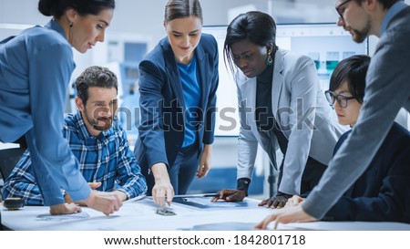 Busy Diverse Team of Computer Engineers and Specialists Gather Around Conference Table, They Discuss Project Drafts and Blueprints, Find Problem Solutions. Industrial Technology Office Meeting Room Royalty-Free Stock Photo #1842801718