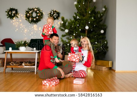 Family mother, father, son and sister in cozy pajamas unpacking gifts at home in the new year's interior near Christmas tree.