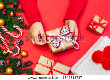 Christmas gifts, children's hands open a new year's gift on a red background, Christmas composition fir branches with gifts, gold-colored decorations, red balls and caramel on a red surface