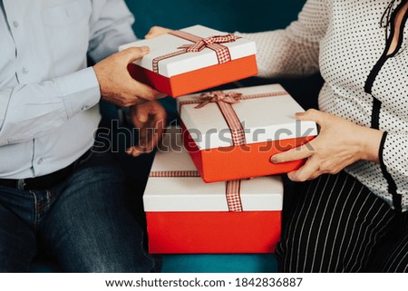 Cropped close up photo of a hands of senior couple is holding a gift boxes. Senior couple celebrating Christmas and exchanging gifts. 