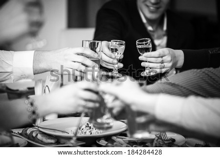 Closeup black and white photo of hands clinking glasses at restaurant
