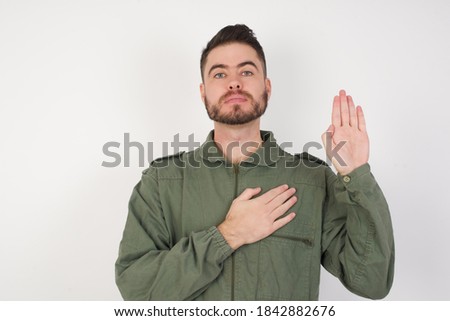 Young caucasian male wearing green overall  isolated over white background Swearing with hand on chest and open palm, making a loyalty promise oath