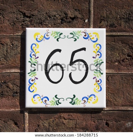 house number sixty five. Hand painted on a white tile.