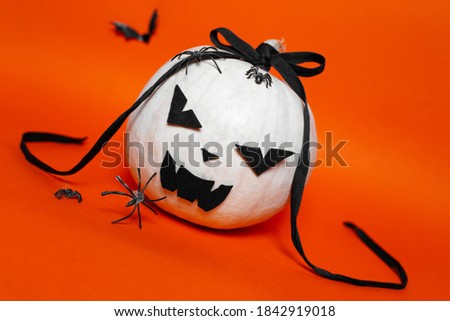 Portrait of white halloween evil pumpkin with black bow on background of orange or lush lava color.