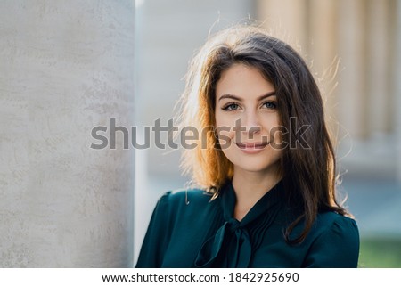 business woman confident smart teacher management student brunette of European appearance standing on the street smiling in a green dress and looking at the camera. Sunny day business center