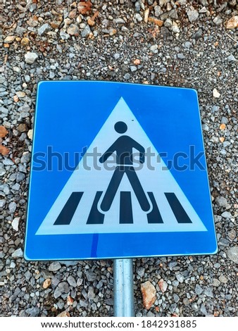 View of pedestrian blue/white sign for crosswalk laying down on the gravel 