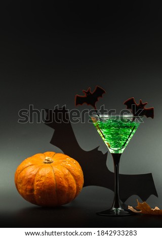cocktail in a glass for a Halloween party, green with decorative bats. Close-up on a black background with an orange pumpkin.