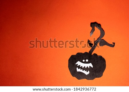 Black colored cut out craft pumpkin with fangs and eyes on an orange background. Pphoto of paper art for your scary Halloween design. There is a place for text.