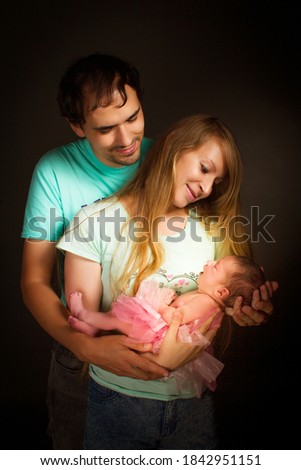 a young couple, a man and a woman, held their newborn daughter in their arms. Studio photo on a black background.