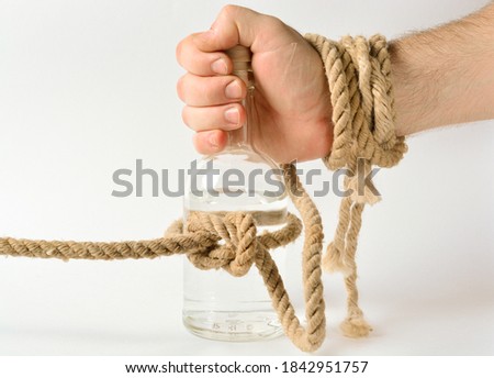 a glass bottle with alcohol is tied in a knot of a rope, a man's hand is trying to take a bottle, the concept of treatment for alcoholism, drunkenness in the family. copy space.