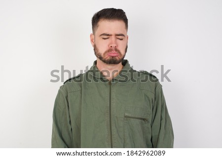 Dismal gloomy rejected Young caucasian male wearing green overall isolated over white background has problems and difficulties, curves lower lip and closes eyes in despair
