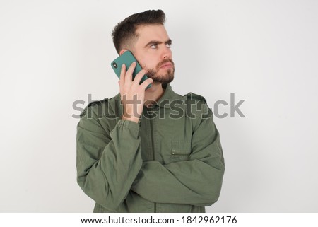 Sad Young caucasian male wearing green overall isolated over white background talking on smartphone. Communication concept.