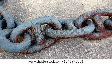line of rusty heavy links of a thick anchor chain, on the ground - closeup of an industrial object in the harbor