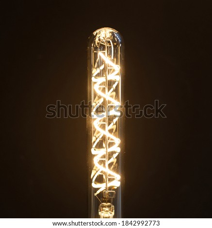 Close up glowing hanging long pipe vintage bulb, long incandescent lamp hanging on brown blurred background, vertical photo