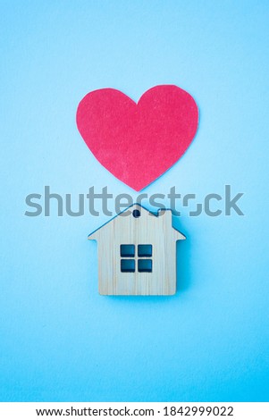 Love home, insurance and mortgage, marriage and valentine concept. Small wooden house toy and paper heart shape on blue background top view vertical