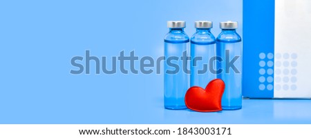 Glass medical ampoules and a red heart on a light blue background. Health concept: medicine, saving lives, covid-19 vaccination, heart treatment. Large format banner with space for text.