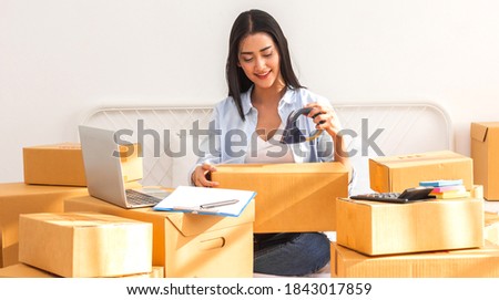 Young smiling beautiful owner asian woman freelancer sme business online shopping working on laptop computer with parcel box on bed at home - SME business online and delivery concept