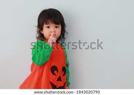 A long-haired Asian girl wearing a green orange fanny pack with pumpkin pattern making fun gestures on a white background.