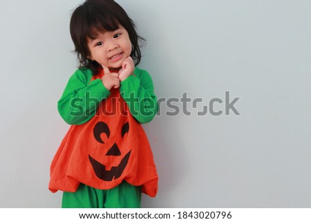 A long-haired Asian girl wearing a green orange fanny pack with pumpkin pattern making fun gestures on a white background.