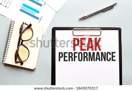 Business concept. Notebook with text PEAK PERFORMANCE sheet of white paper for notes, glasses in the white background