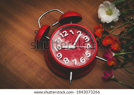 red clock and flowers on wooden background