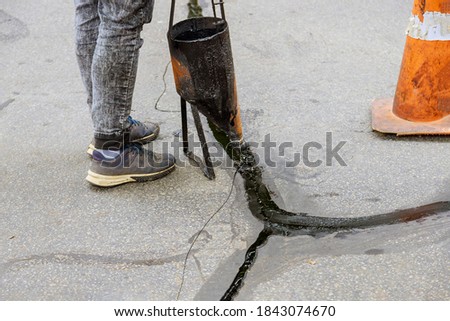 Man sealing asphalt driveway with filled cracks sealcoating selective focus Royalty-Free Stock Photo #1843074670