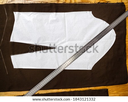 top view of steel ruler laying on a layout of sewing patterns of dress on brown fabric on wooden table at home