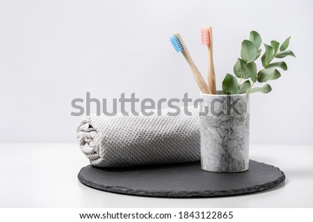 Concept of biodegradable objects. Two bamboo toothbrush in cup near bathroom towel and eucalyptus plant on black plate stand against white copy space background. Oral and dental care Royalty-Free Stock Photo #1843122865