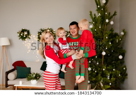 Father and little son and doughter in cozy pajamas unpacking gifts at home in the new year's interior near Christmas tree.