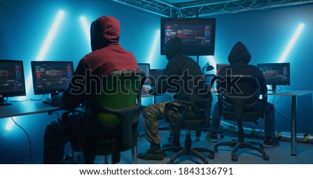 Tracking shot of man in hoodie joining group of hackers sitting in small hidden cabin in dark field Royalty-Free Stock Photo #1843136791