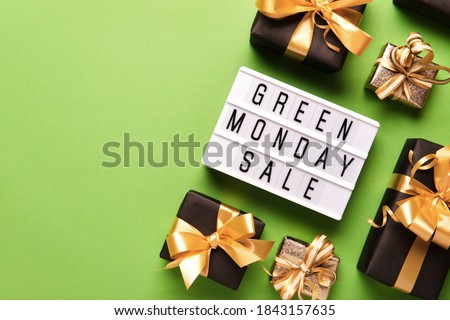 Lightbox with GREEN MONDAY SALE text on green paper background with black gift boxes and golden bow, copy space.