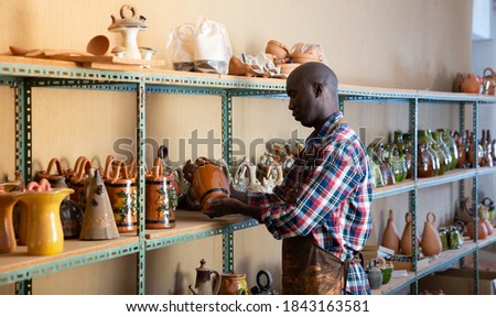 Afro-american artisan in apron having ceramics in store warehouse. High quality photo
