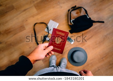 A man holds a Russian passport with a backpack and travel accessories in the background. The concept of travel. Photo from above.