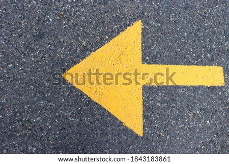 Horizontal image. One-way arrow in yellow on gray concrete. The arrow points to the left. Blank space for text.