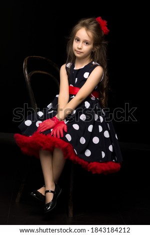 Girl Wearing Polka Dot Dress Sitting on Chair with Crossed Legs