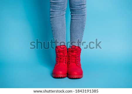 Cropped photo of slim lady legs standing alone wear stylish expensive red shoes boots sneakers denim jeans isolated blue color background