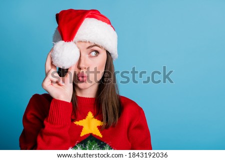 Portrait photo of young millennial girl wearing christmas cap keeping holding white soft cotton ball in hand looking at side with pouted plump lips sending air kiss isolated on blue color background