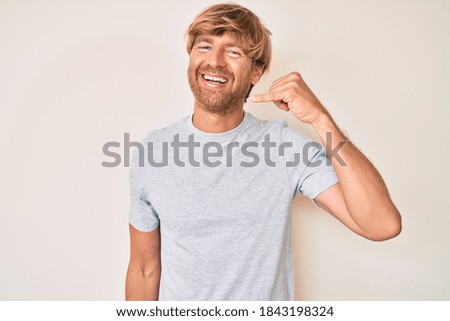 Young blond man wearing casual clothes smiling doing phone gesture with hand and fingers like talking on the telephone. communicating concepts. 