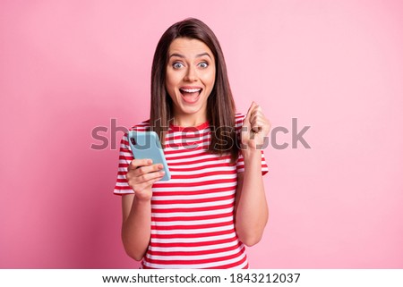 Photo portrait of girl wearing striped t-shirt keeping smartphone gesturing like winner isolated on pastel pink color background