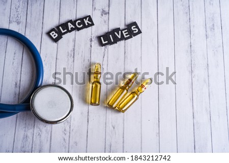 stethoscope and medical ampoules and inscription black lives on a white wood background