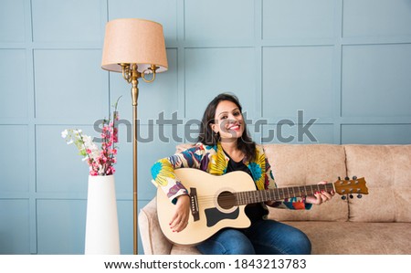 Pretty Asian Indian young woman musician performing while taking online music class or recording video on smartphone