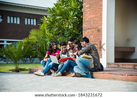 Young Asian Indian college students reading books, studying on laptop, preparing for exam or working on group project while sitting on grass, staircase or steps of college campus Royalty-Free Stock Photo #1843231672