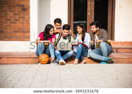 Young Asian Indian college students reading books, studying on laptop, preparing for exam or working on group project while sitting on grass, staircase or steps of college campus Royalty-Free Stock Photo #1843231678