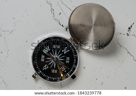 An old compass with an iron lid with scratches on the textured surface of the table. Selective focus.