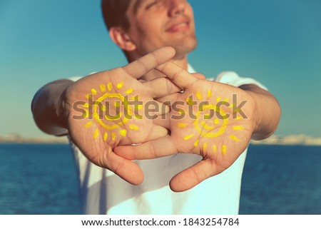 mens hand with paint yellow sun face and smile against blue sky, copy space, close up Royalty-Free Stock Photo #1843254784