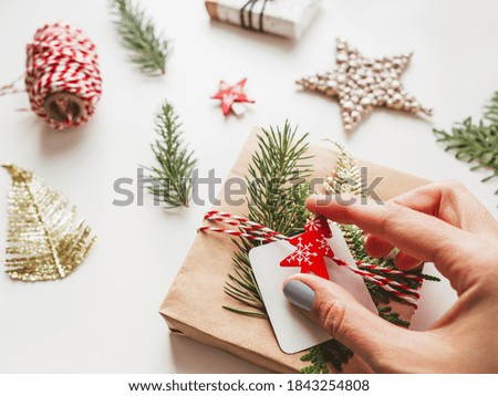 DIY presents wrapped in craft paper with fir tree twigs and red symbol of Christmas tree. Top view on decorations on New Year gifts. Festive background. Winter holiday spirit. 