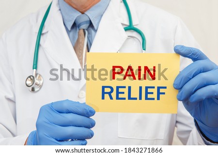 Close-up of a male doctor in gloves holding a sign with the text PAIN RELIEF